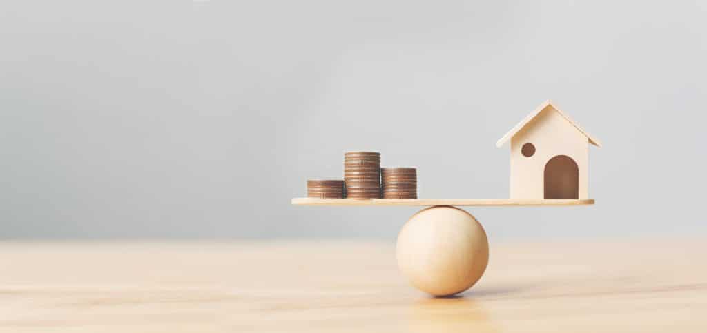 Maison en bois en équilibre face à des pièces de monnaie : estimer le juste prix de sa maison